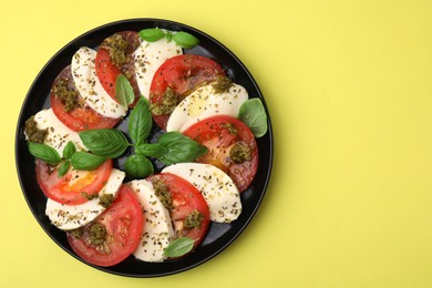Photo of Plate of delicious Caprese salad with pesto sauce on yellow table, top view. Space for text