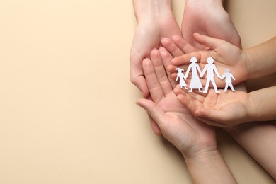 Photo of Parents and child holding paper cutout of family on beige background, top view. Space for text