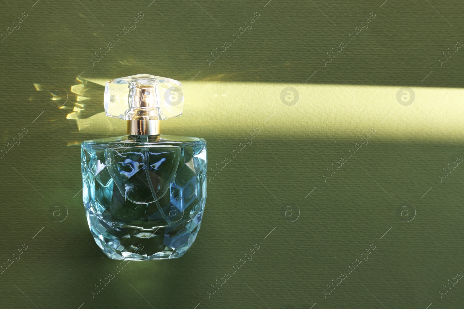 Photo of Luxury women's perfume. Sunlit glass bottle on olive background, top view. Space for text