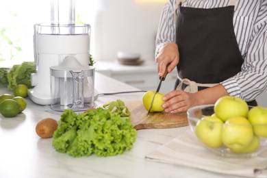 Young woman cutting fresh apple for juice at table in kitchen, closeup