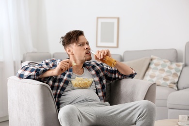 Lazy man with bottle of beer and chips watching TV at home