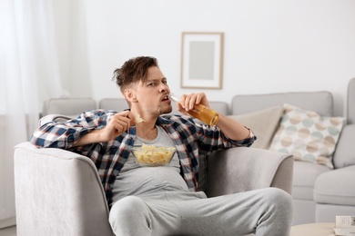 Photo of Lazy man with bottle of beer and chips watching TV at home