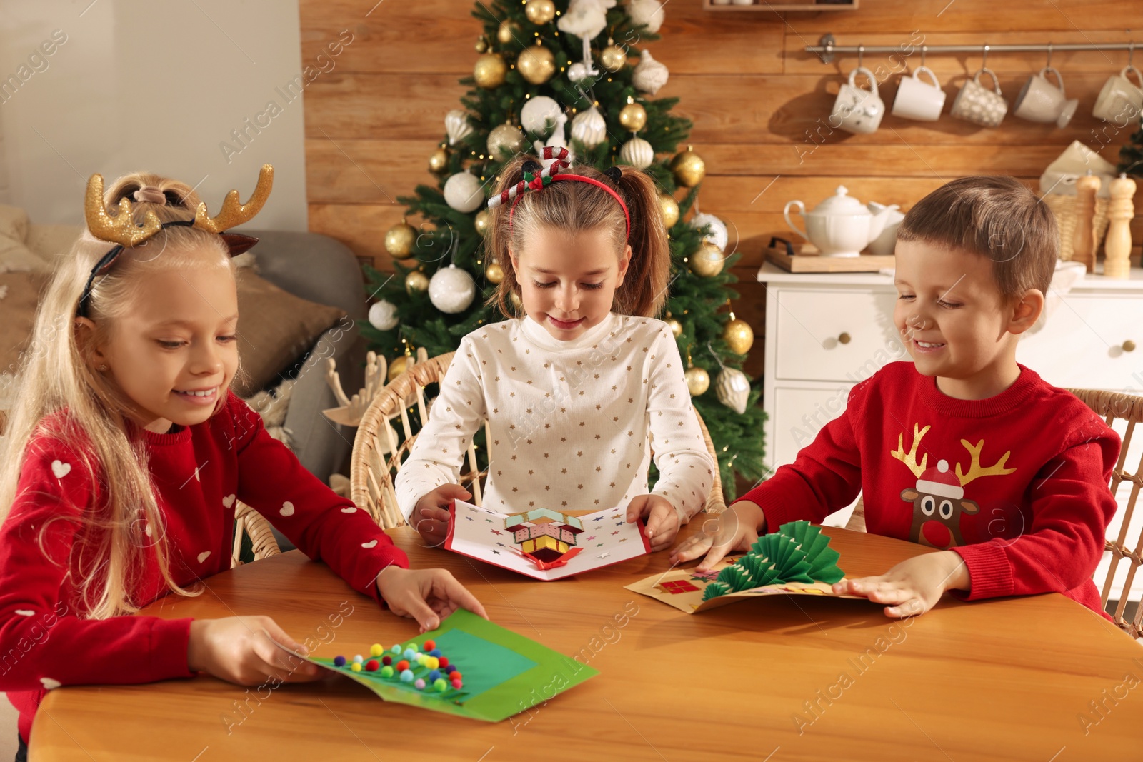 Photo of Cute little children with beautiful Christmas cards at table in decorated room