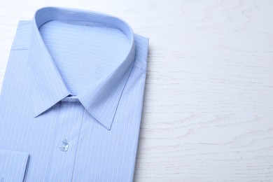 Photo of Stylish light blue shirt on white wooden table, top view with space for text. Dry-cleaning service