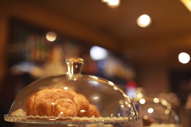 Photo of Glass cloche and plate with croissants on counter in cafe. Space for text