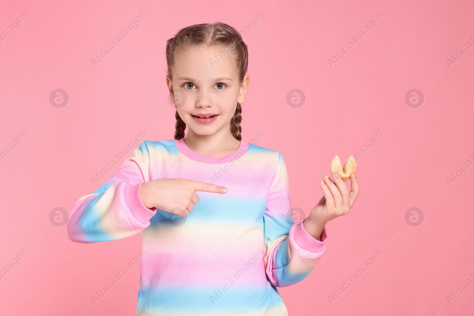 Photo of Girl pointing at tasty fortune cookie with prediction on pink background