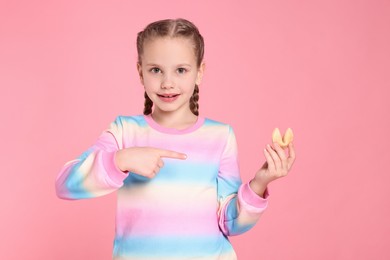 Photo of Girl pointing at tasty fortune cookie with prediction on pink background