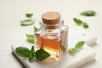 Photo of Bottle of essential basil oil and fresh leaves on white wooden table