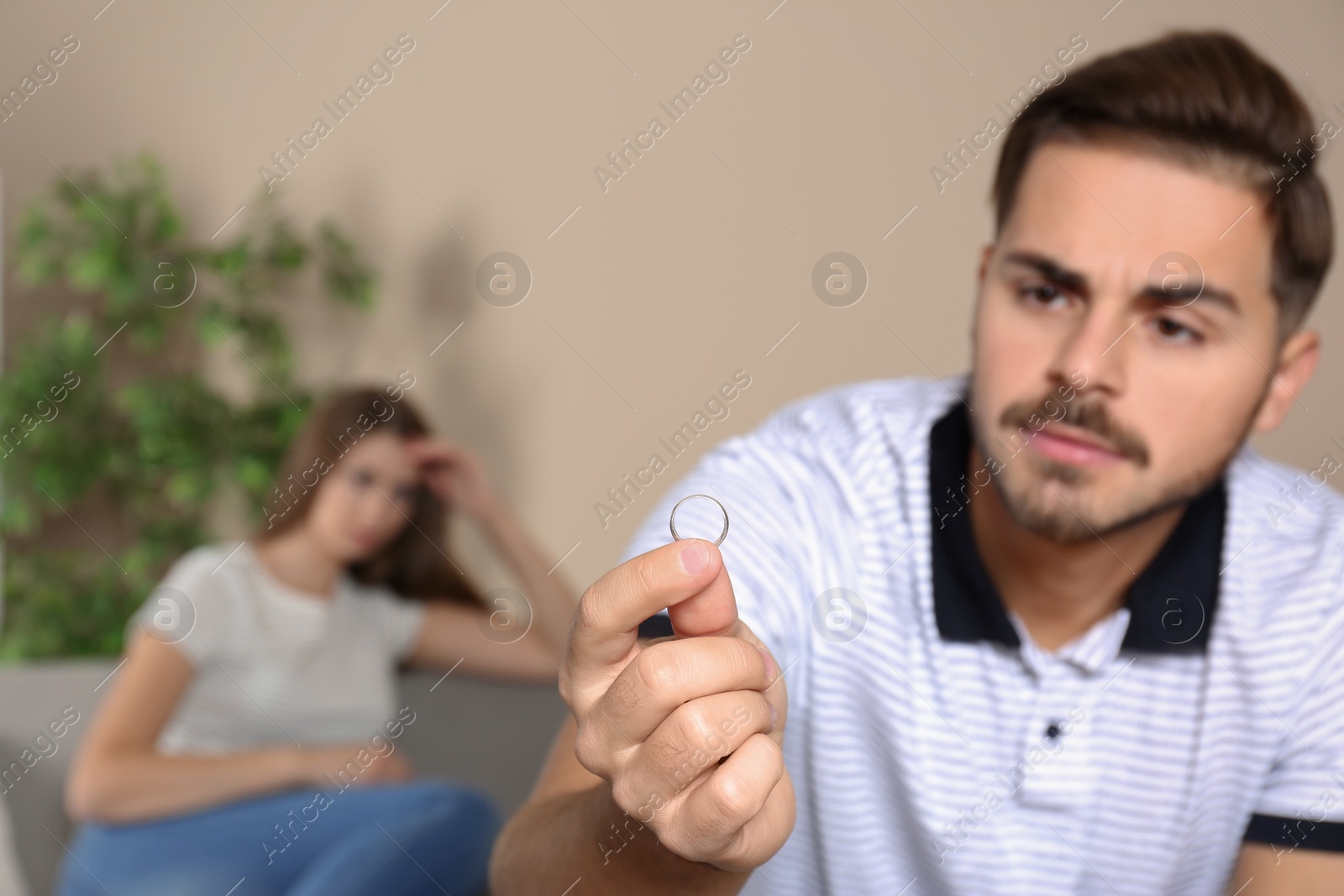 Photo of Young man looking on wedding ring after conflict with his wife at home. Relationship problems