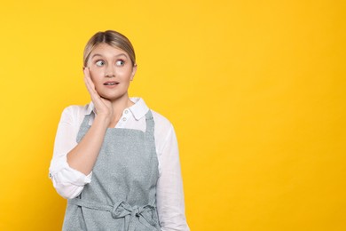 Photo of Beautiful young woman in clean apron with pattern on orange background. Space for text