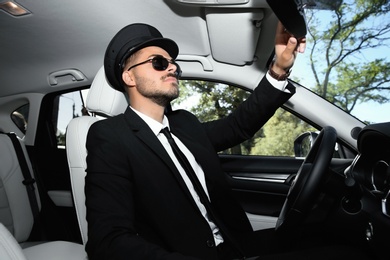 Photo of Young handsome driver adjusting interior mirror in luxury car