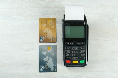 New modern payment terminal and credit cards on white wooden table, flat lay