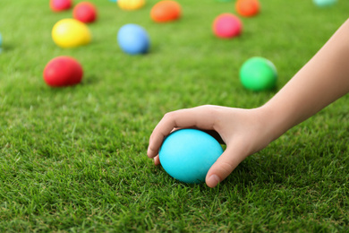 Little child taking Easter egg from green grass, closeup
