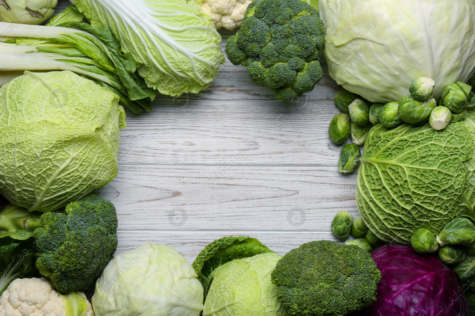 Photo of Frame of different cabbages on white wooden table, flat lay. Space for text