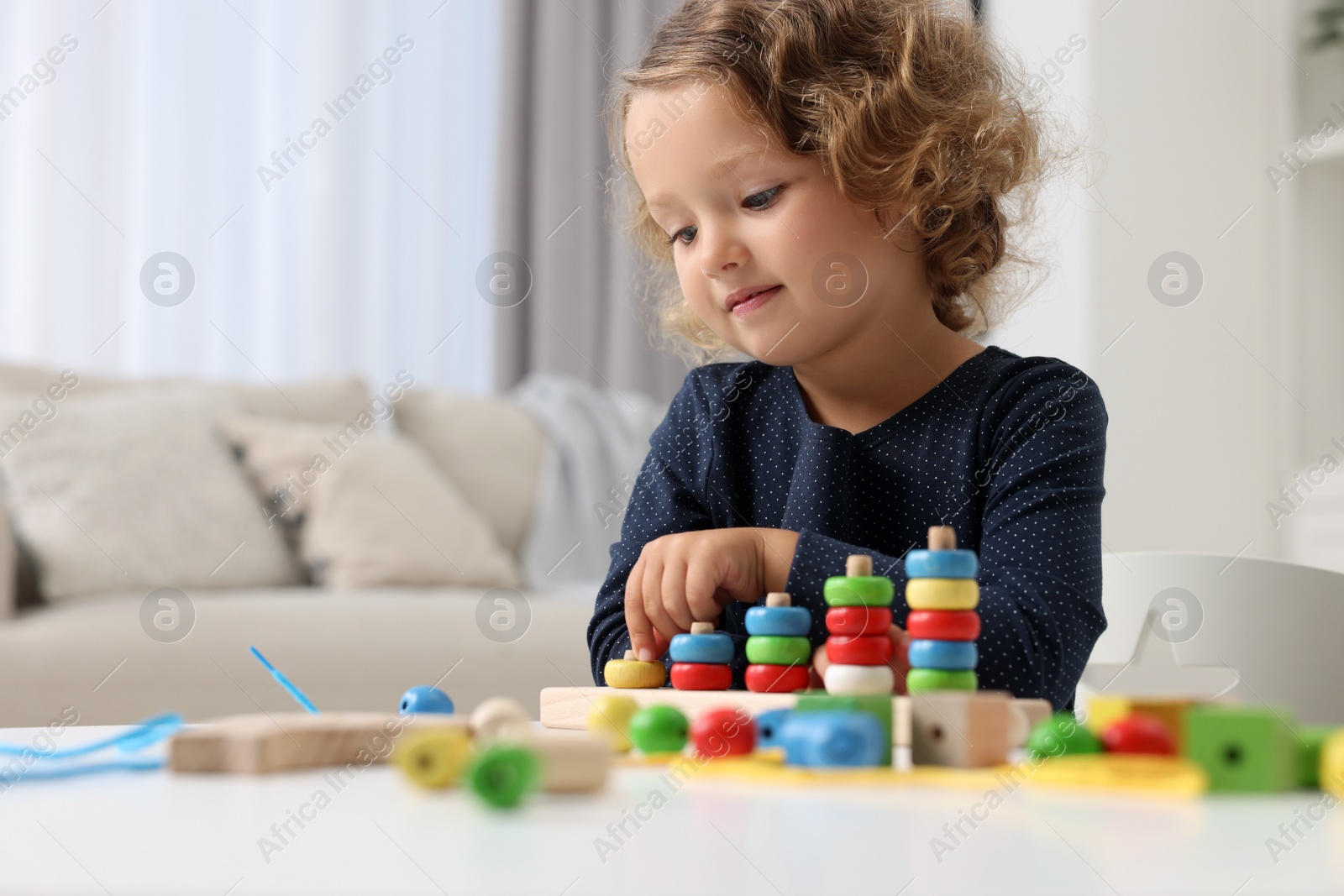 Photo of Motor skills development. Little girl playing with stacking and counting game at table indoors