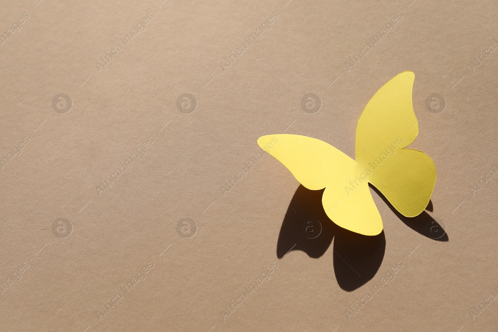 Photo of Yellow paper butterfly on light brown background, above view. Space for text