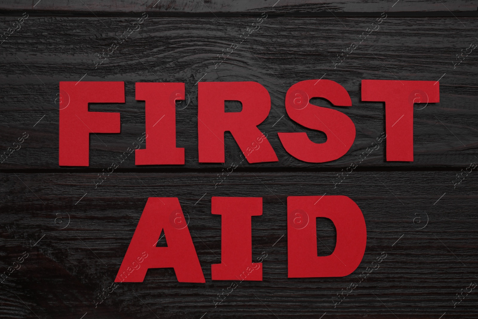 Photo of Words First Aid made of red letters on black wooden table, flat lay