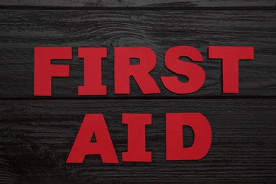 Photo of Words First Aid made of red letters on black wooden table, flat lay