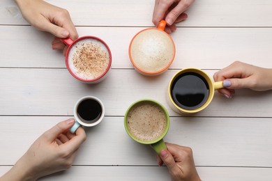 People holding different cups with aromatic hot coffee at white wooden table, top view