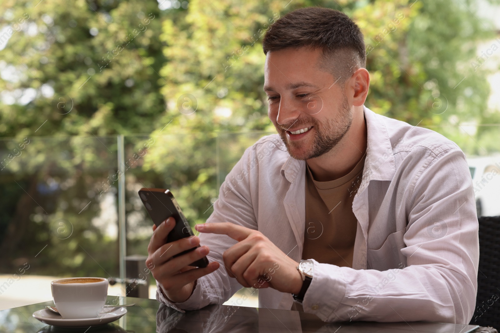 Photo of Handsome man typing message on smartphone at table in outdoor cafe