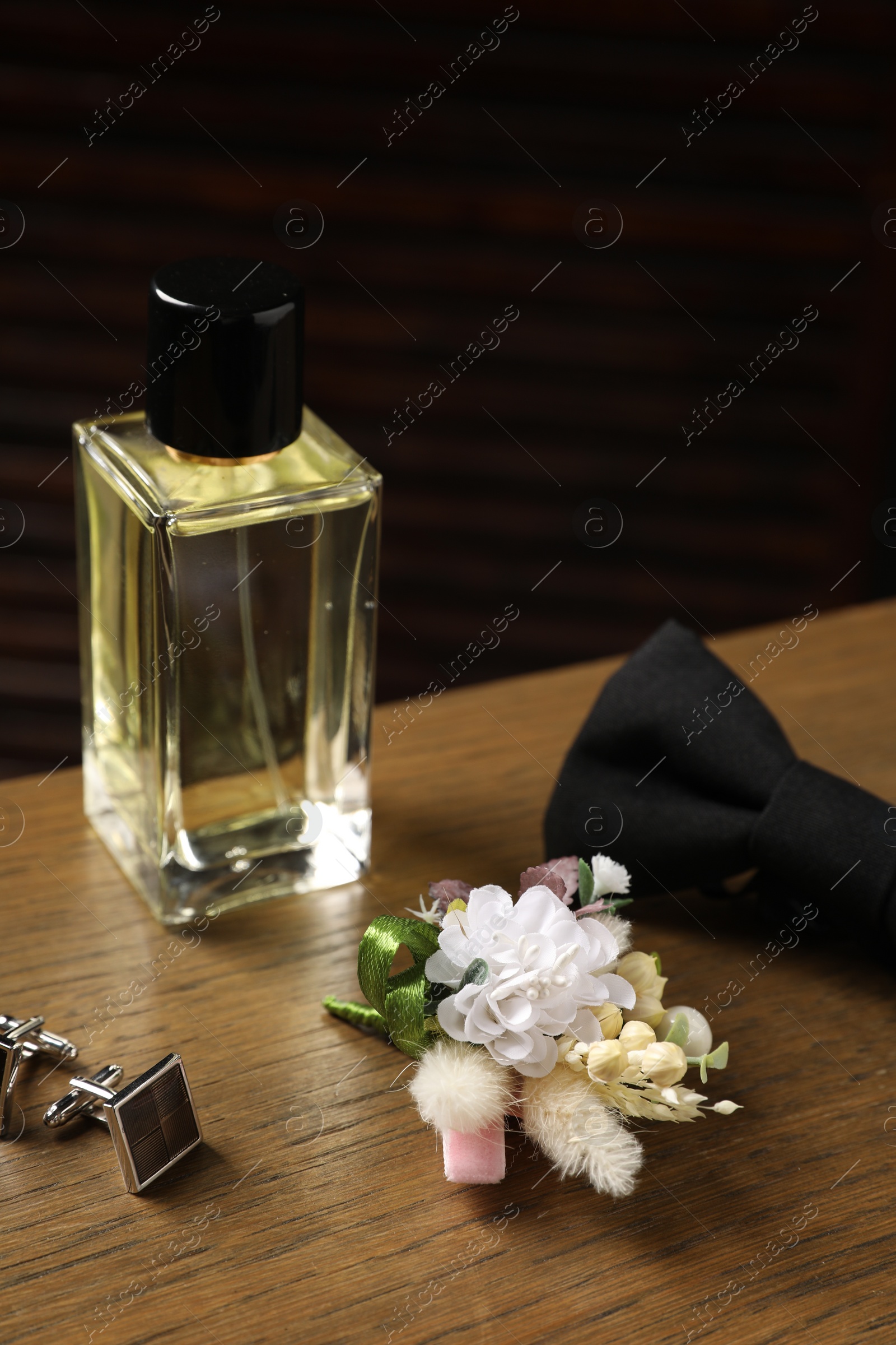 Photo of Wedding stuff. Stylish boutonniere, perfume bottle, bow tie and cufflinks on wooden table, closeup