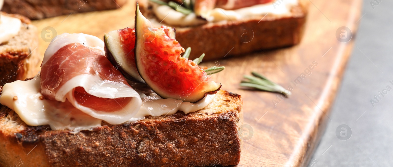 Image of Bruschettas with cream cheese, prosciutto and figs served on wooden board, closeup. Banner design 