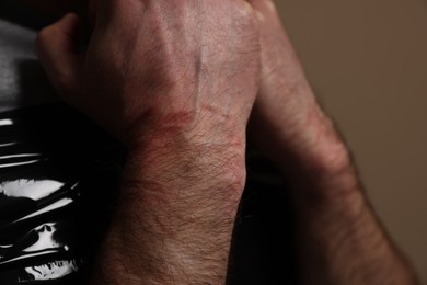 Photo of Tied man with bruises on beige background, closeup. Hostage taking