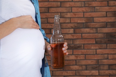 Photo of Future mother with bottle of alcohol drink against brick wall, closeup. Bad habits during pregnancy