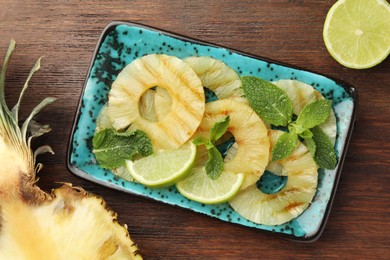 Photo of Tasty grilled pineapple slices, mint and cut lime on wooden table, flat lay