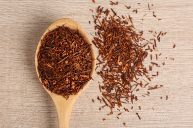 Photo of Spoon with dry rooibos leaves on wooden table, flat lay