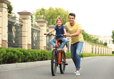 Photo of Dad teaching son to ride bicycle outdoors