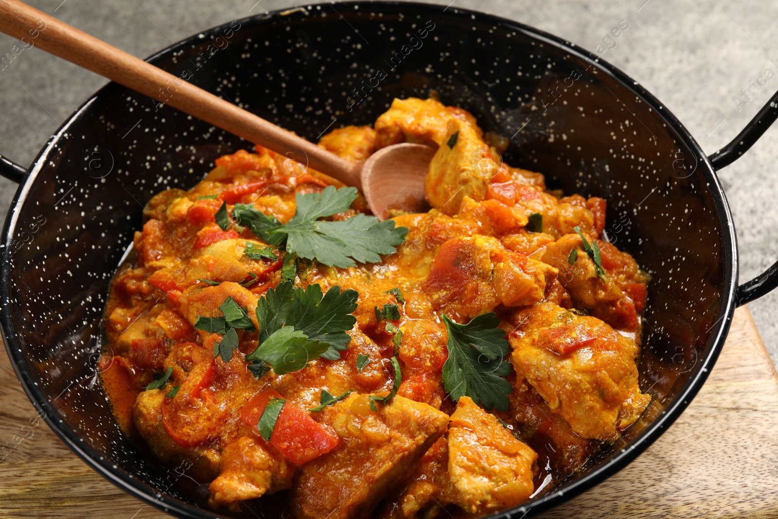 Photo of Delicious chicken curry in frying pan and spoon on table, closeup