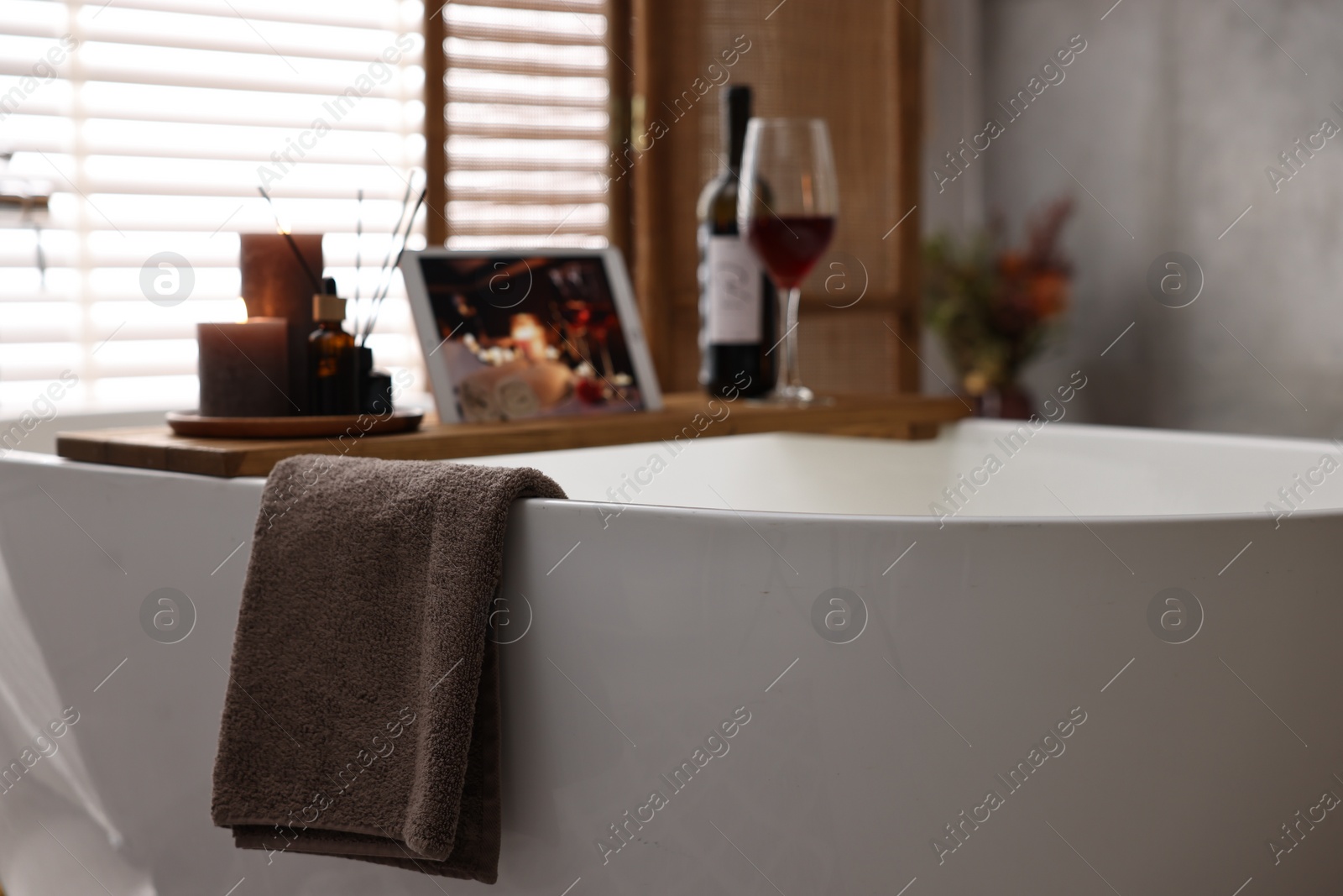 Photo of Towel and wooden tray with spa products on bathtub in bathroom, selective focus