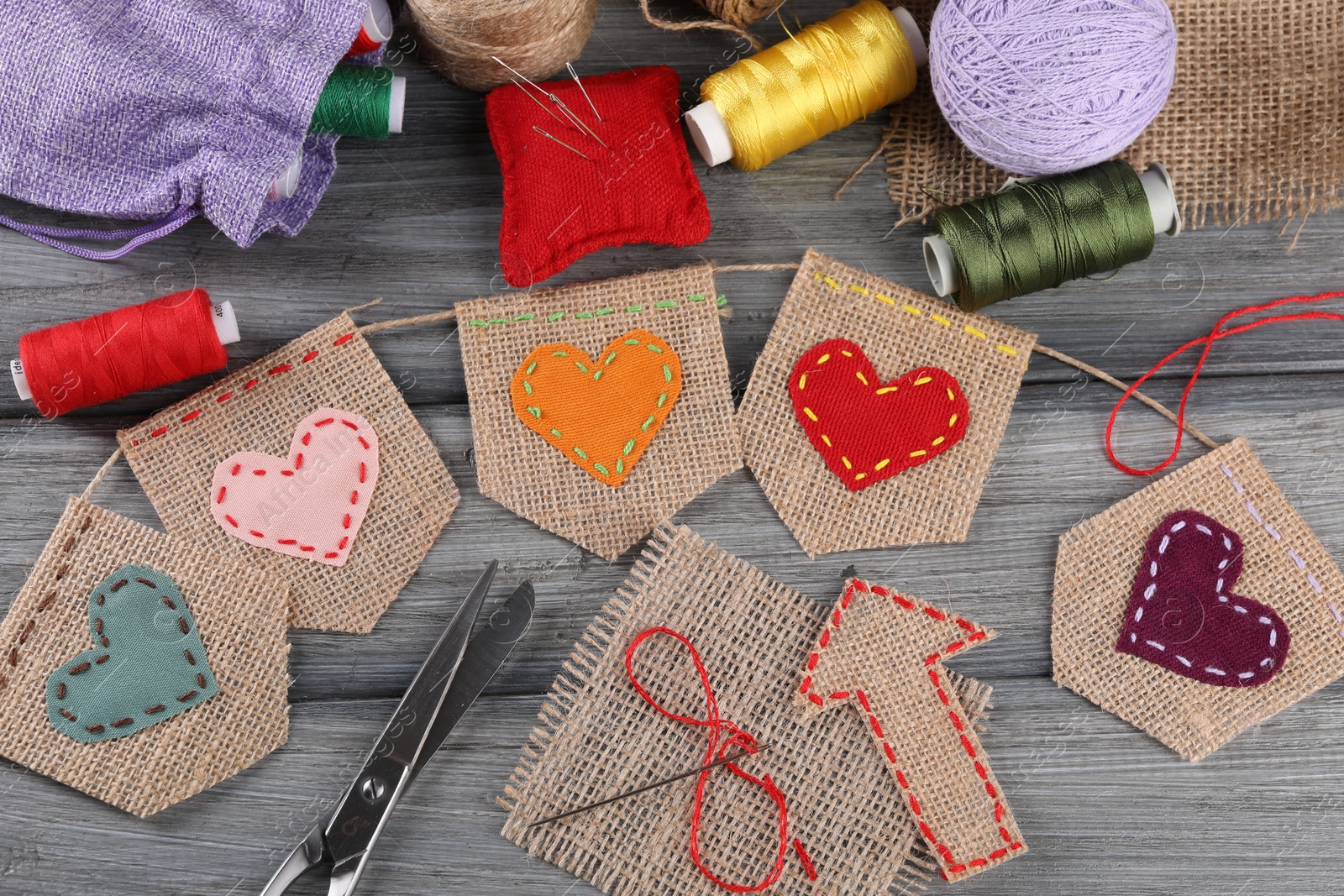 Photo of Bunting flags made with burlap fabric and sewing tools on grey wooden table, flat lay