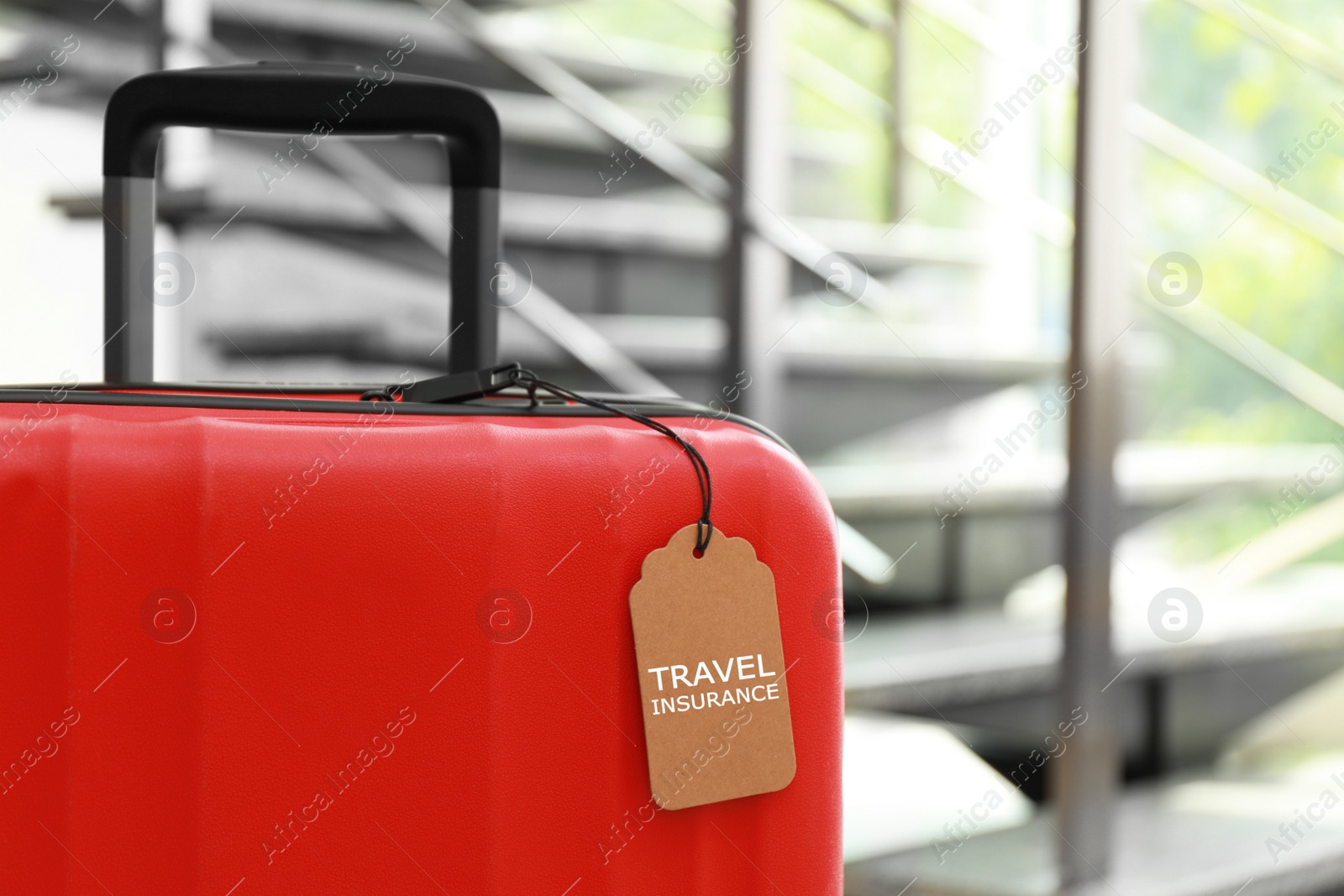 Photo of Red suitcase with TRAVEL INSURANCE label at stairs indoors, space for text