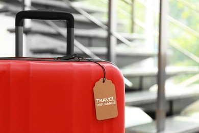 Red suitcase with TRAVEL INSURANCE label at stairs indoors, space for text