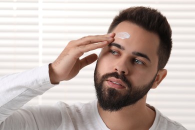Photo of Man with dry skin applying cream onto his forehead indoors