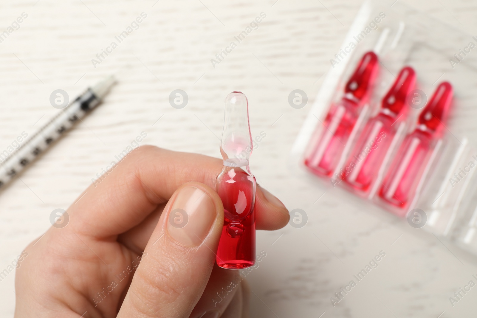 Photo of Woman holding pharmaceutical ampoule with medication at white wooden table, top view