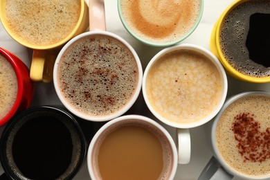 Photo of Many cups with different aromatic coffee on white table, flat lay