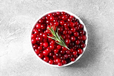 Fresh ripe cranberries and rosemary in bowl on grey table, top view