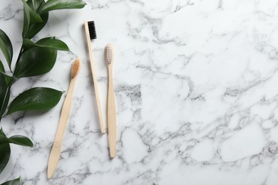 Bamboo toothbrushes and green branch on white marble table, flat lay. Space for text