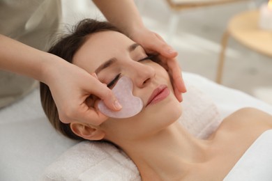 Young woman receiving facial massage with gua sha tool in beauty salon