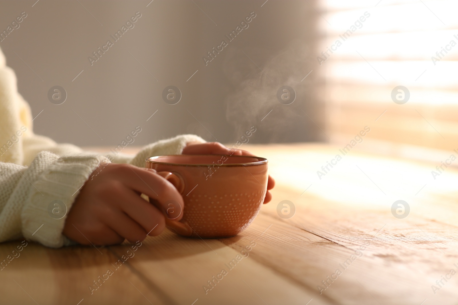 Photo of Woman with cup of tasty coffee at wooden table, closeup. Good morning