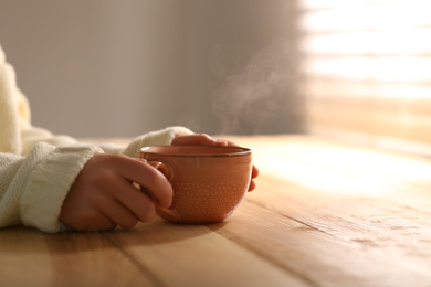 Photo of Woman with cup of tasty coffee at wooden table, closeup. Good morning