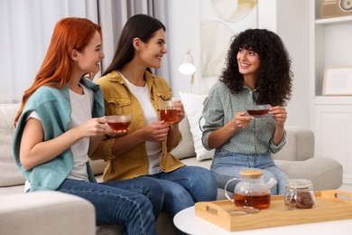 Photo of Happy young friends with cups of tea spending time together at home