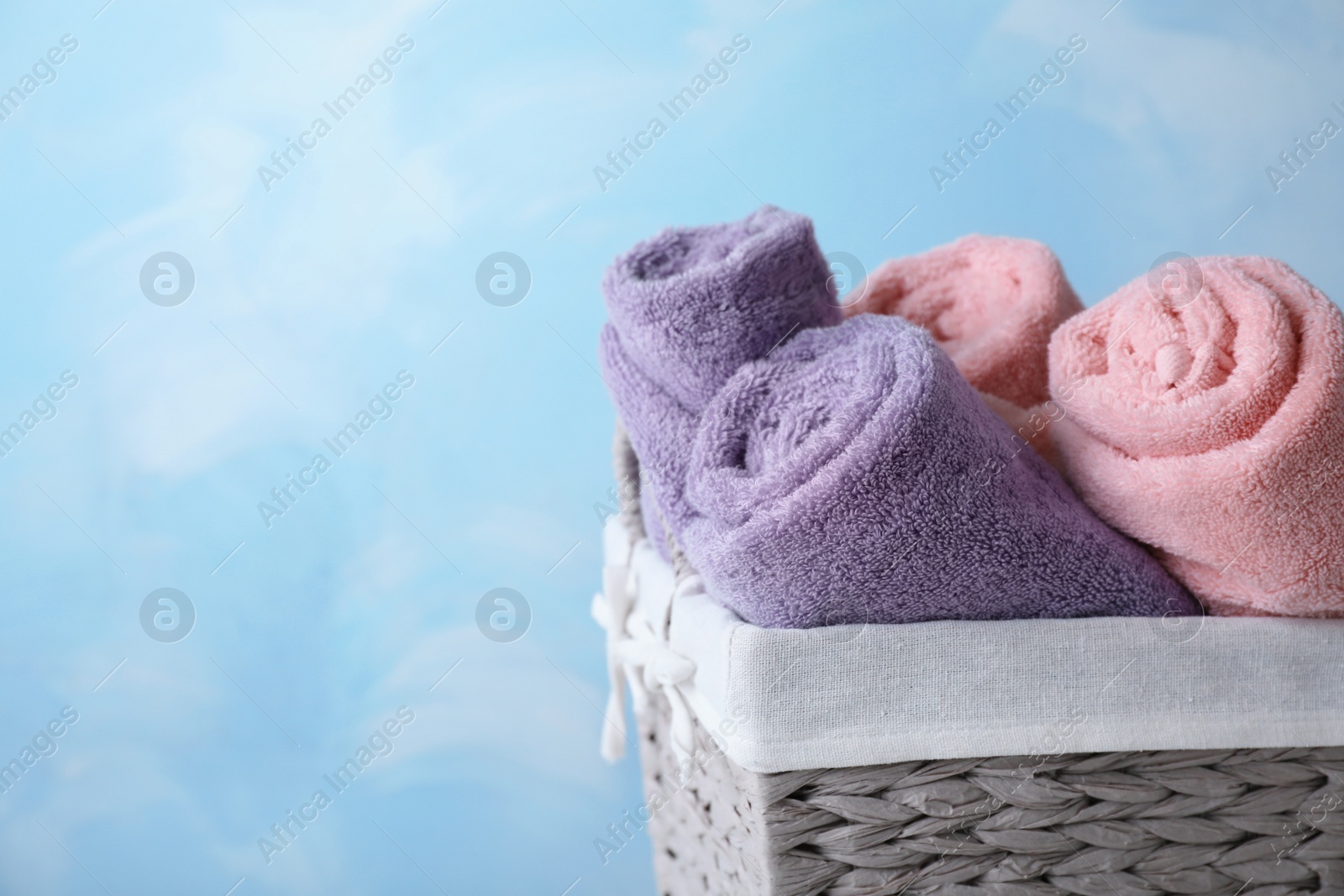 Photo of Basket with soft bath towels on color background. Space for text