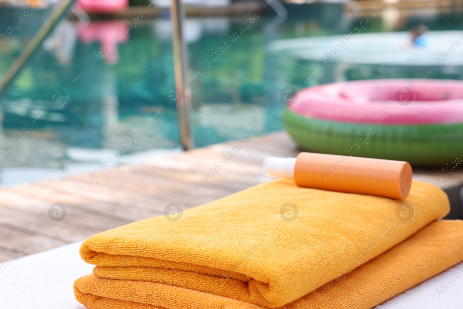 Photo of Beach towels and sunscreen on sun lounger near outdoor swimming pool at luxury resort. Space for text