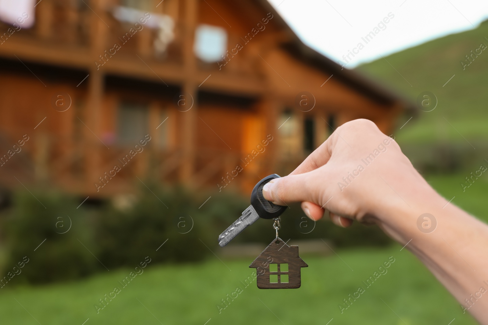 Photo of Real estate agent holding key and blurred house on background. Focus on hand