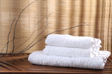 Photo of Stacked soft towels on wooden table and tree branches indoors