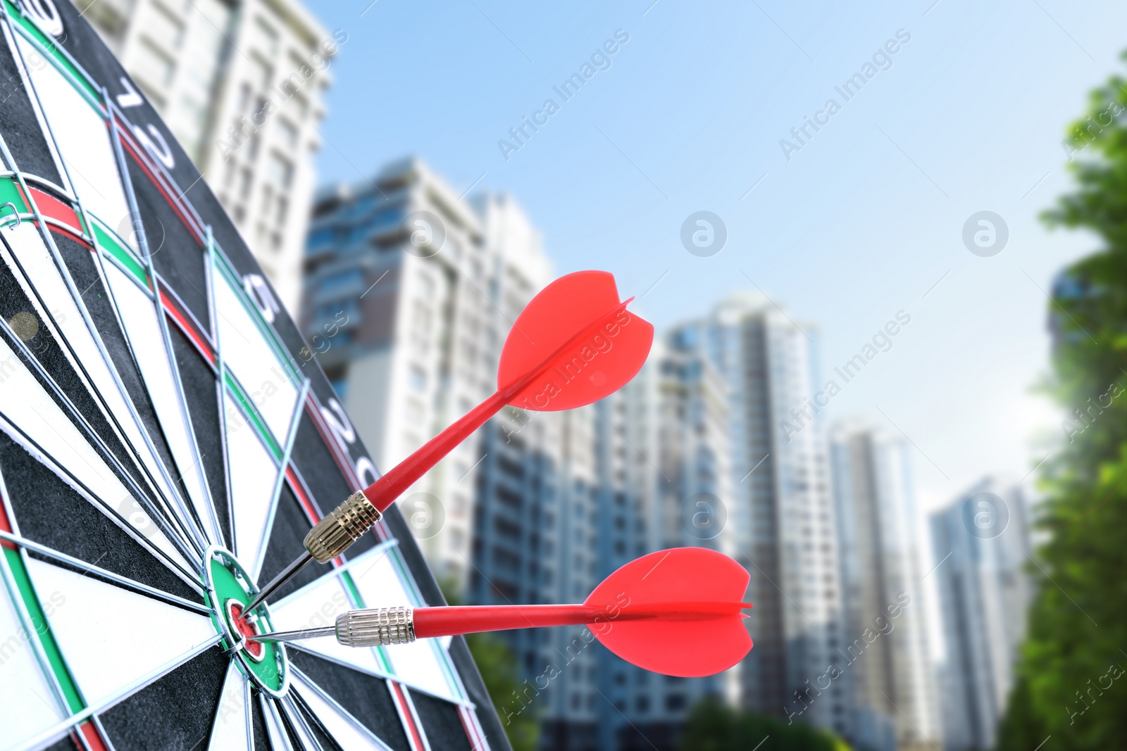 Image of Board with red darts hitting target against blurred of view cityscape